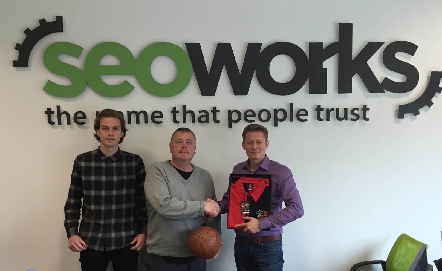 three members of The SEO Works team stood in front of logo on the wall behind