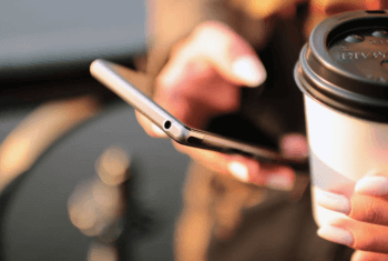 woman holding an iphone in one hand and a coffee in the other hand