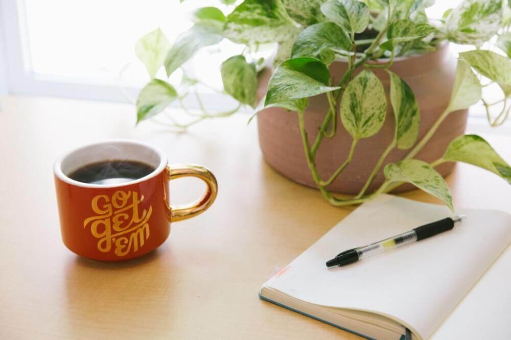 a notebook and pen next to a mug of black coffee